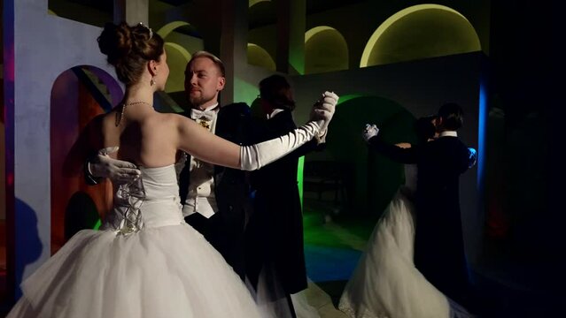elegant gentlemen and stunning ladies are dancing waltz in dark ballroom, slow motion shot
