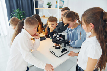 Girl looking into microscope. Group of children students in class at school with teacher