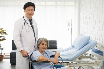 Obraz premium Portrait of male doctor and elderly patient woman sit on wheelchair. Male doctor visit or taking care elderly asian woman on wheelchair at the hospital. People and health care concept