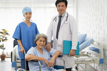 Portrait of doctor, nurse and elderly patient woman sit on wheelchair. Male doctor and female nurse visit or taking care elderly asian woman on wheelchair at the hospital