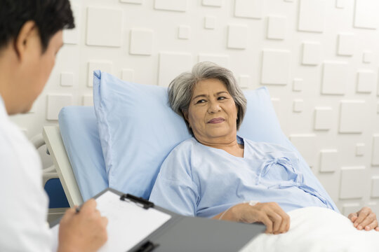 Male doctor and elderly patient woman on bed. Male doctor visit and writing note to seek advice with elderly asian woman on bed at the hospital. People and health care concept