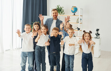 Showing hello gestures. Group of children students in class at school with teacher