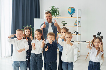 Showing thumbs up. Group of children students in class at school with teacher