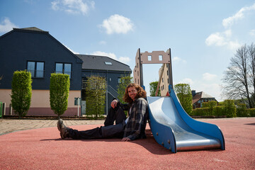A cheerful young Caucasian man sitting near the kids slides in the playground