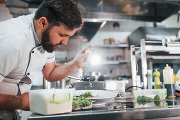 Man poring some salt. Professional chef preparing food in the kitchen
