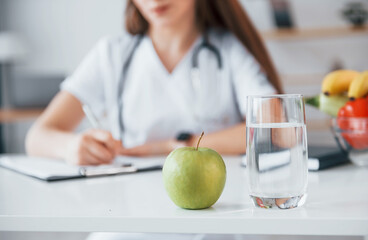 Woman writing information into the notepad. Professional medical worker in white coat is in the office