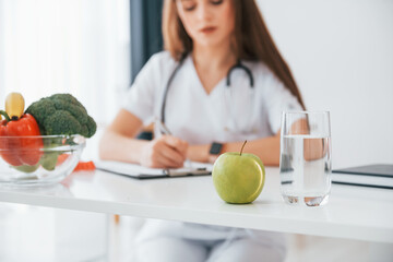 Woman writing information into the notepad. Professional medical worker in white coat is in the...