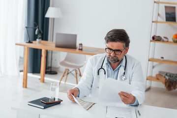 Man is busy with documents. Professional medical worker in white coat is in the office