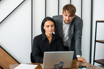 a man and a woman in the office are working at a laptop and smiling