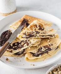 Pancakes with chocolate cream and nuts on a white plate. Thin pancakes, pancakes. Delicious breakfast or snack. The background of the food recipe. Vertical orientation.