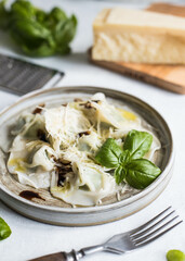 Spinach-stuffed ravioli garnished with balsamic sauce, grated parmesan and young basil leaves. Restaurant serving. Close-up.