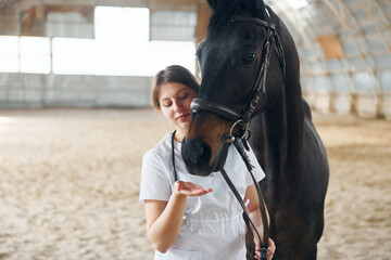 Front view. Female doctor in white coat is with horse on a stable