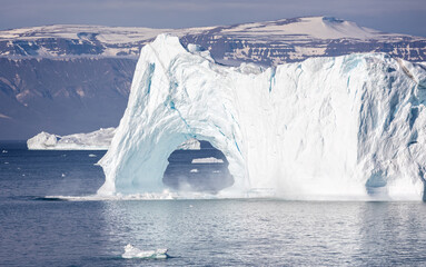 Large iceberg wirh arch part of which has fallen into the water in Disko Bay, Greenland