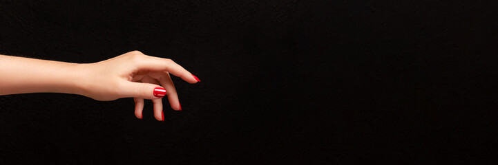 Female hand with beautiful manicure - red nails on dark black background with copy space banner....