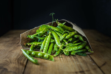 Pods of green peas and pea on a dark wooden surface. Horizontal orientation
