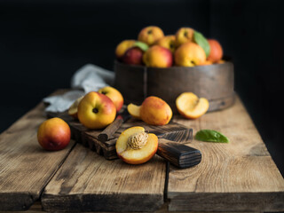 Peaches with leaves on dark wooden board with peach in halves with peach seed stone. Composition with ripe juicy peaches Harvest for food. Fresh organic fruit