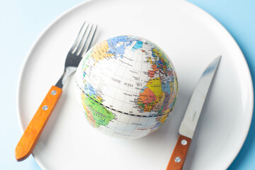 Globe on a plate with fork and knife on a light background, world food day concept