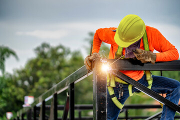 Welders wear safety belts and plastic helmets to weld steel structures.
