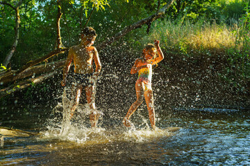 children playing in the river. A girl and boy raises her hands up in the water and splashes water...