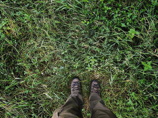 Man with field clothing and footwear standing on green grass field, point of view. 