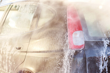 car in foam at a self-service car wash. close-up. man washing car with water spray