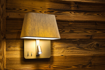 Beside lamp mounted on a wooden wall. Alpine-style hotel room interior. Beside lamp in a rustic...