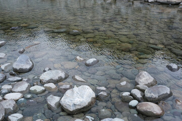 Background of rounded river stones of different sizes in the water. River bank