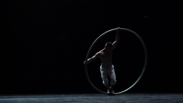 Muscular circus artist perform Cyr Wheel on a black background. Concept of Individuality and creativity 