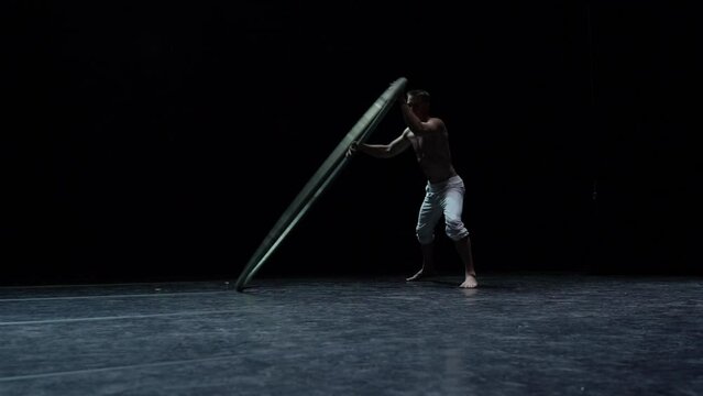 Muscular circus artist perform Cyr Wheel on a black background. Concept of originality, creativity and outstanding
