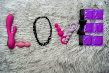the word love made of sex toys and condoms on gray fur background, concept of seduction, introduction to couple game, i love you phrase