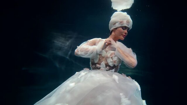 amazing fairy lady is floating underwater in magical sea or lake, woman in white gown is swimming