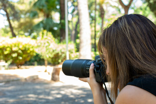 Young Girl Passionate in Photography that shoots with a telezoom in an Italian Natural Park in a sunny day on Blurred Background
