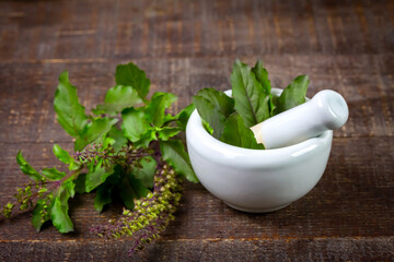 Tulsi or Holy basil leaf in mortar with pestle on rustic wooden table. Tulsi is used in ayurvedic medicine.