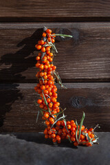 Branch of sea buckthorn berries on a wooden brown background, a branch in the shape of the letter L, copy space, the concept of a healthy diet