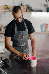 Fototapeta na wymiar Artisan sculptor artist mixing paint in his workshop. Pink paint, paint mixer