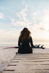 Rear View Of Female Surfer At The Beach Sitting On Jetty With Surfboard