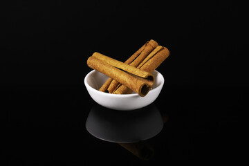Cinnamon sticks in a white plate on a dark table with reflection. Close-up