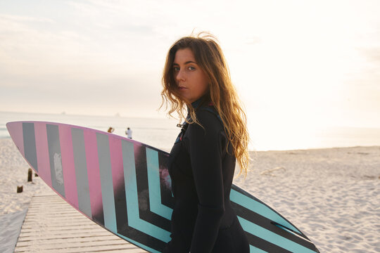 Female Surfer At The Beach Walking Down Jetty With Surf Board Or Kite Surfing Wearing Wetsuit