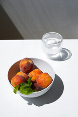 Close-up of a bowl of fresh appetizing peaches in daylight next to a glass of water.