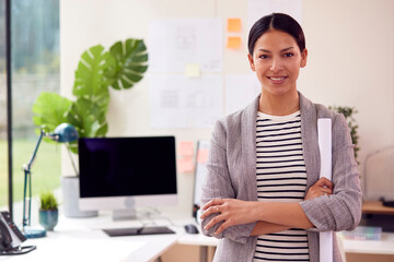 Portrait Of Female Architect Standing In Office Holding Rolled Up Building Plans