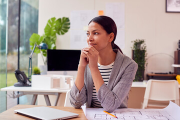 Thoughtful Female Architect In Office Sitting At Desk Working On Plans For New Building On Laptop