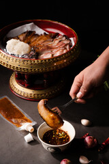 Close up fork pick up and dip a piece of grill pork jowl in spicy sauce thai food with sticky rice