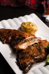 Close up cut in half grilled bbq ribs serve in white square plate on black table