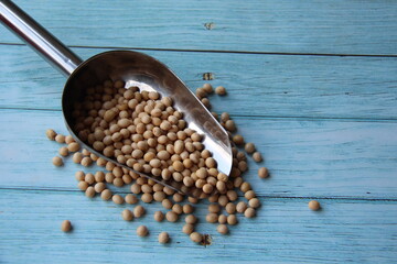 Soybeans (Glycine max) in a stainless steel measuring spoon, isolated, selective focus on wooden table, protein concept.