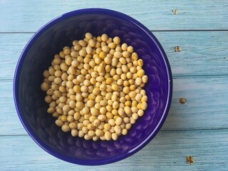 Soybeans in grains (Glycine max) in blue crockery bowl isolated on wooden table, top view, protein concept.