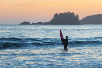 Surfer with surf board on Chesterman Beach, Tofino, Vancouver Island, Canada.