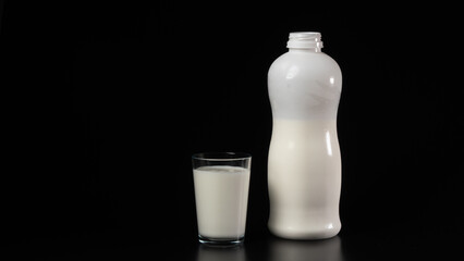 A glass of milk next to the bottle on a black background