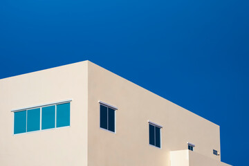 Minimal geometric architecture background of blue glass windows on pale yellow office building against blue clear sky in low angle and perspective side view