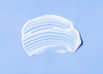 The texture of white cream on blue background. A smear of moisturizer closeup. Lotion swatch. Beauty, skin care product smear smudge drop. SPF sunscreen cream sample