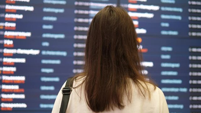 Girl looks at the information board at the airport and looks for her flight.